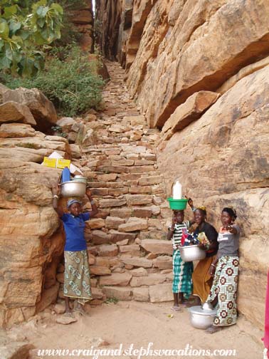 Dogon women approach the cliffside staircase Dogon women approach the cliffside staircase