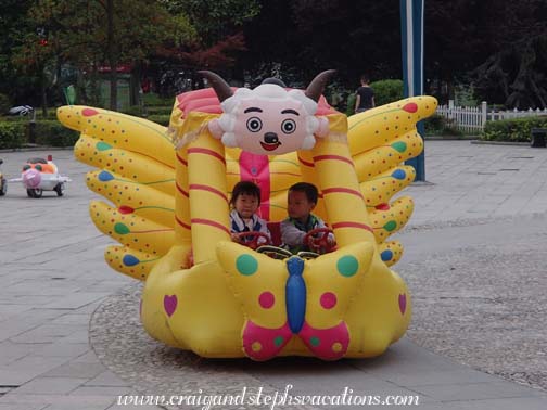 Two kids go for a ride in a whimsical Year of the Sheep vehicle in Kaili square