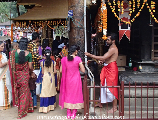 Priest blesses a woman by touching a sword to her head, Periayanampetta Bhagavathy Temple