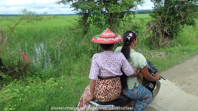 Ladies riding a scooter past rice paddies