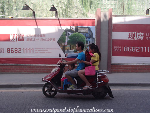 Family of 4 on a scooter (Note the little girl sitting on a plastic stool) Family of 4 on a scooter (Note the little girl sitting on a plastic stool)