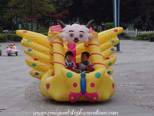 Two kids go for a ride in a whimsical Year of the Sheep vehicle in Kaili square