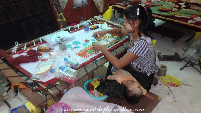 Mother embroiders a kalaga while her toddler sleeps, Aung Nan Handicrafts Workshop Mother embroiders a kalaga while her toddler sleeps, Aung Nan Handicrafts Workshop